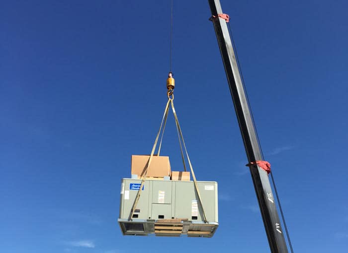 Crane lifting a commercial AC unit onto a rooftop
